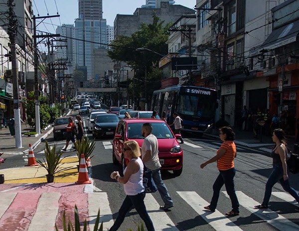 People crossing street on crosswalk. Bus behind them. Sunny day